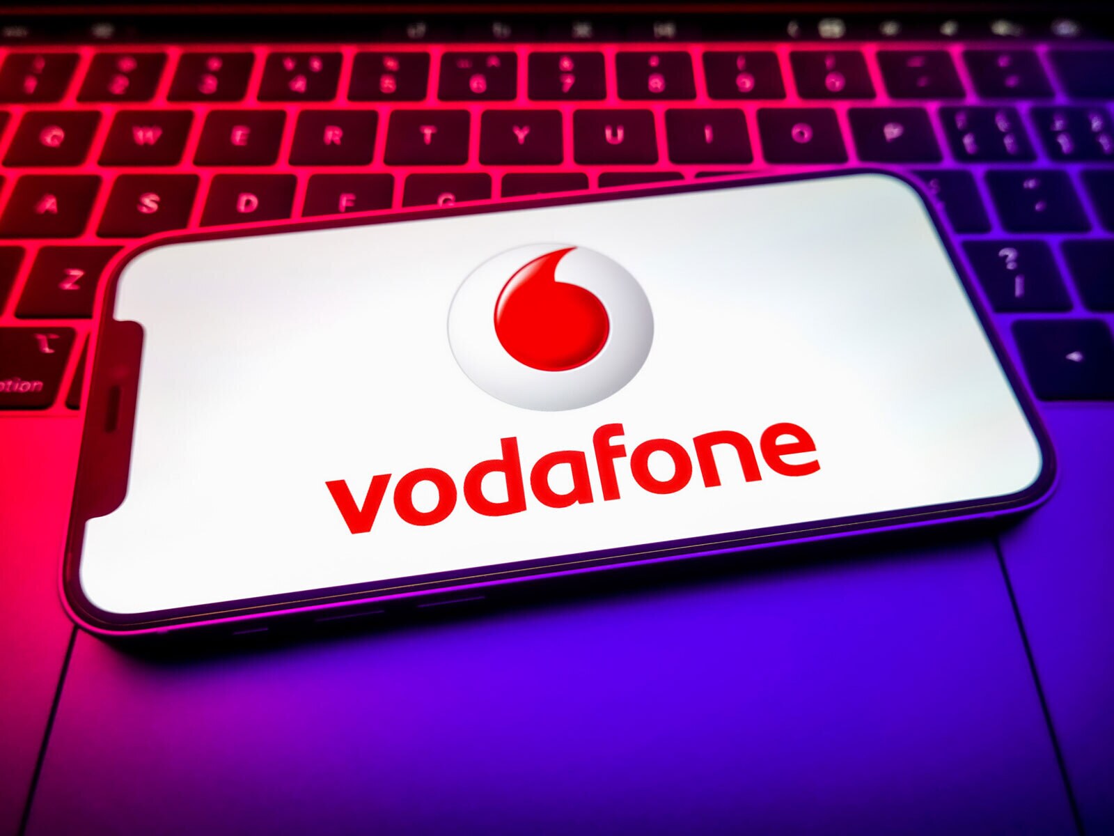 The Vodafone 'quotation mark' logo appears on a smartphone screen in front of a laptop keyboard.