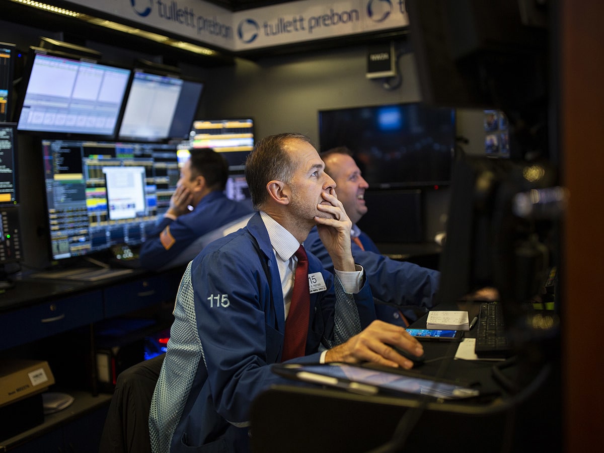 traders sit looking as screens on trading desk in New York