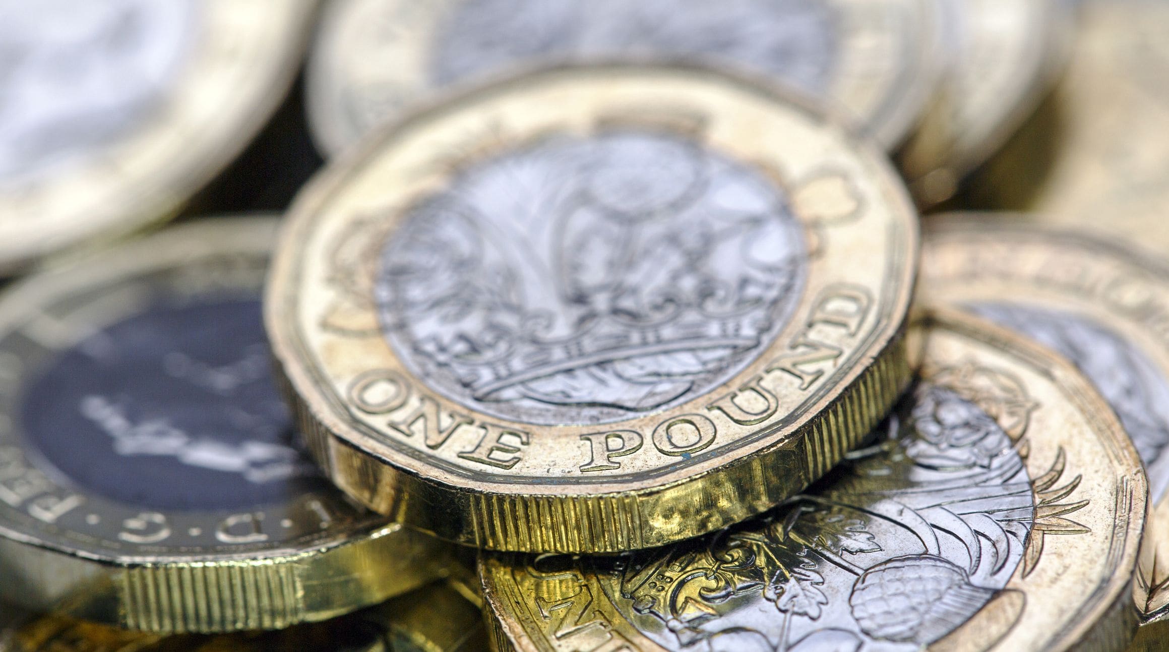 Image shows a close-up of a pile of £1 coins.