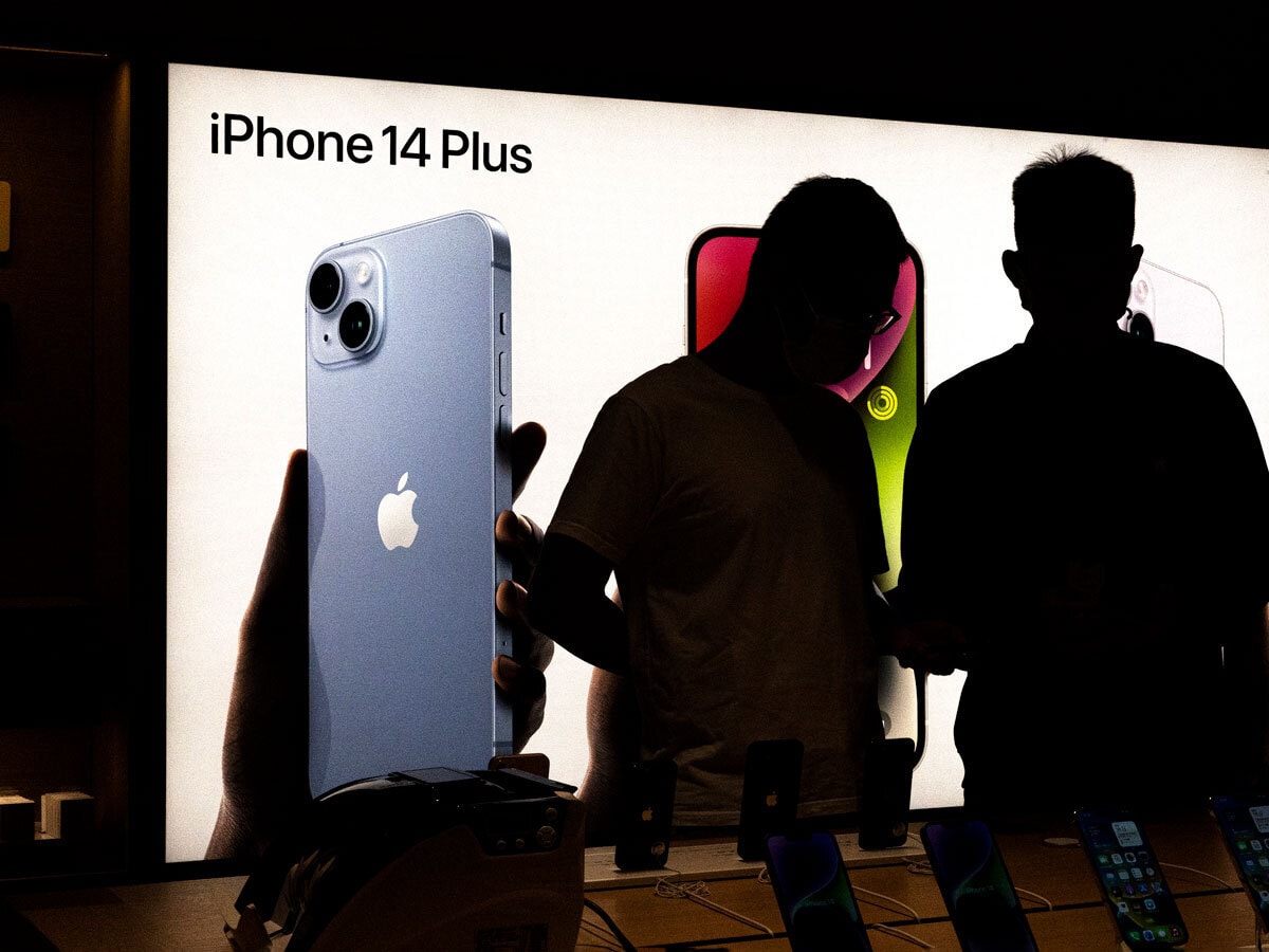 Apple share price: Two silhouetted figures stand in front of an advertising board for the new iPhone 14 Plus.
