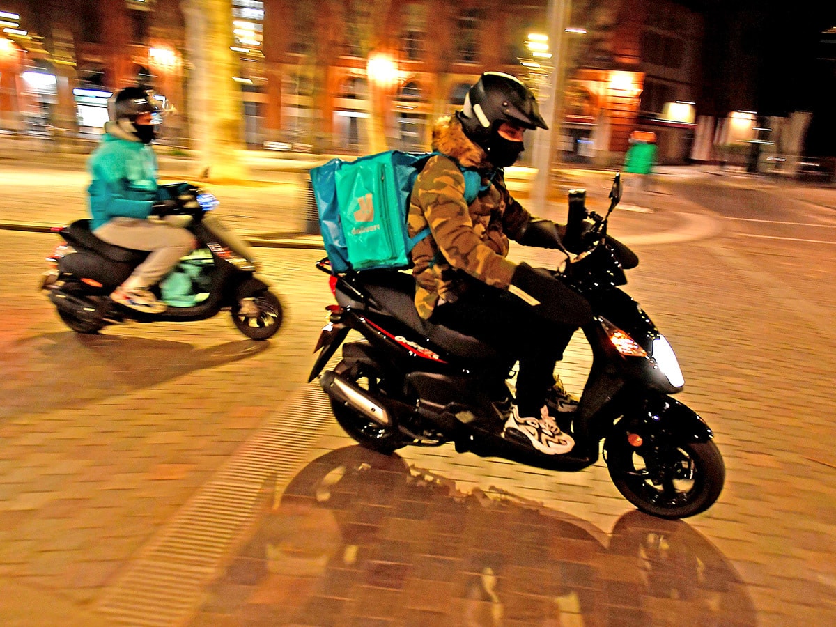 Deliveroo share price: Delivery drivers carrying Deliveroo backpacks ride their motorcycles at night.