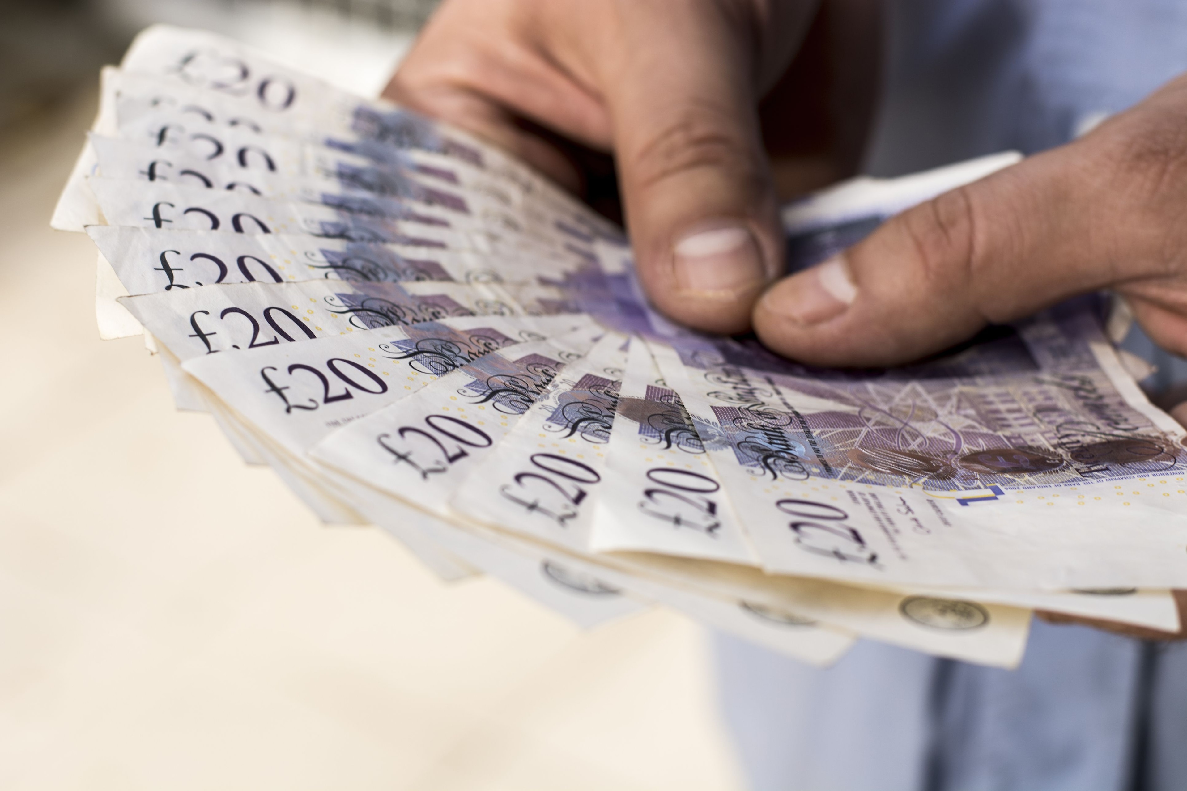 A close-up shot of someone holding a spread of £20 notes.