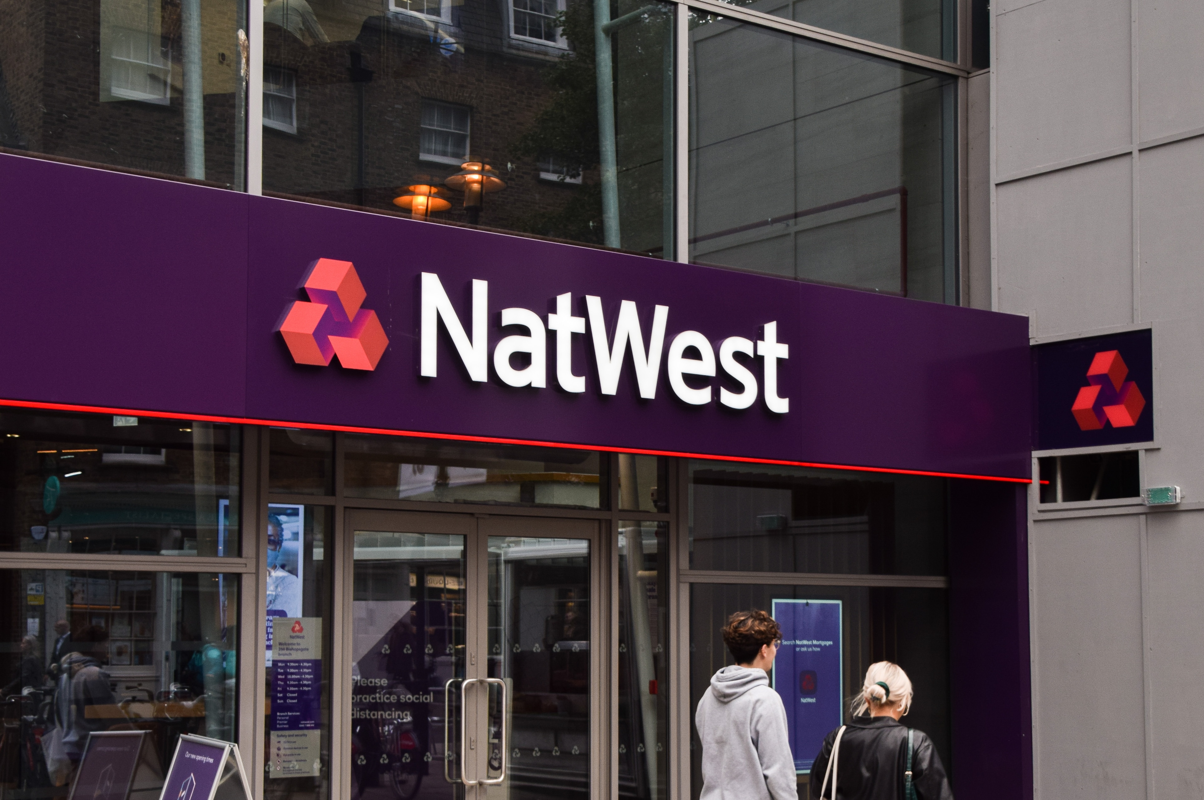 NatWest share price: pedestrians walk past the entrance to a branch of NatWest.