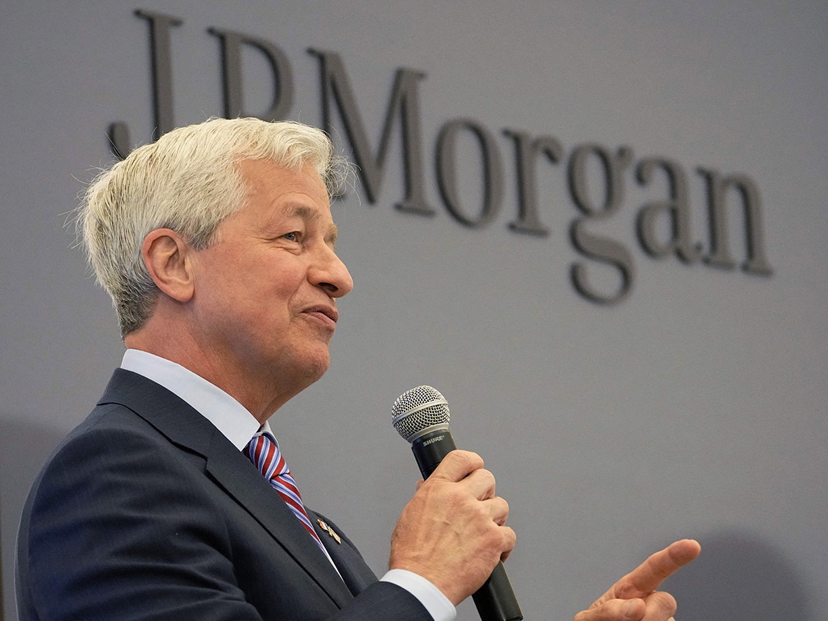 JPMorgan share price: JPMorgan CEO Jamie Dimon speaks into a microphone, backed by a sign displaying the JPMorgan logo.