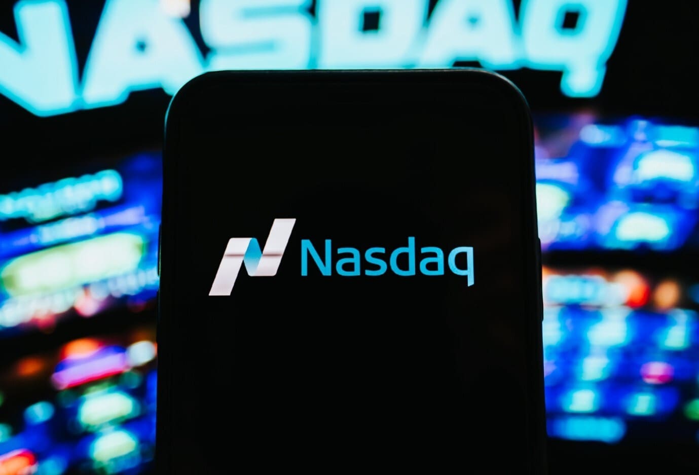 A smartphone displays the Nasdaq logo against a background of financial charts.