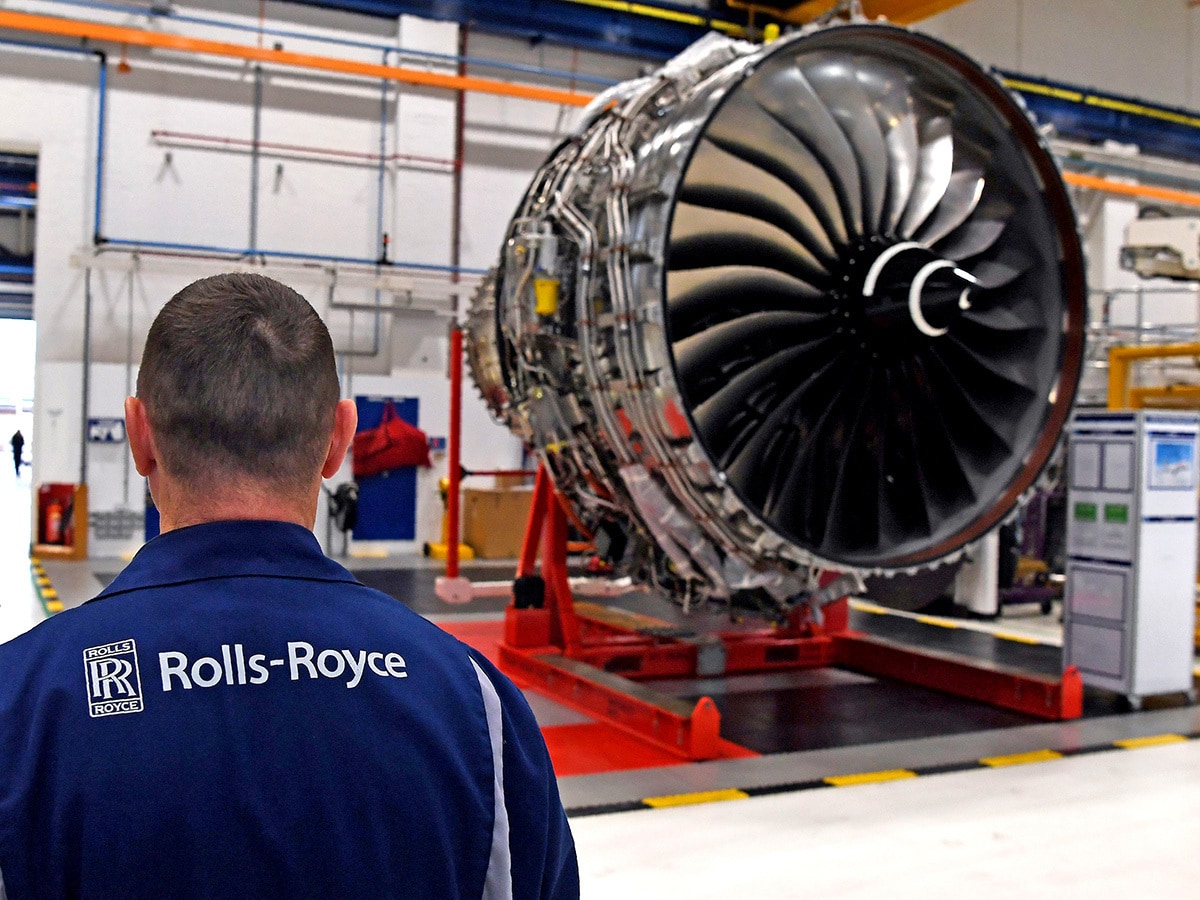 Rolls-Royce share price: A worker in Rolls-Royce-branded clothing stands in front of a Rolls-Royce aircraft engine.