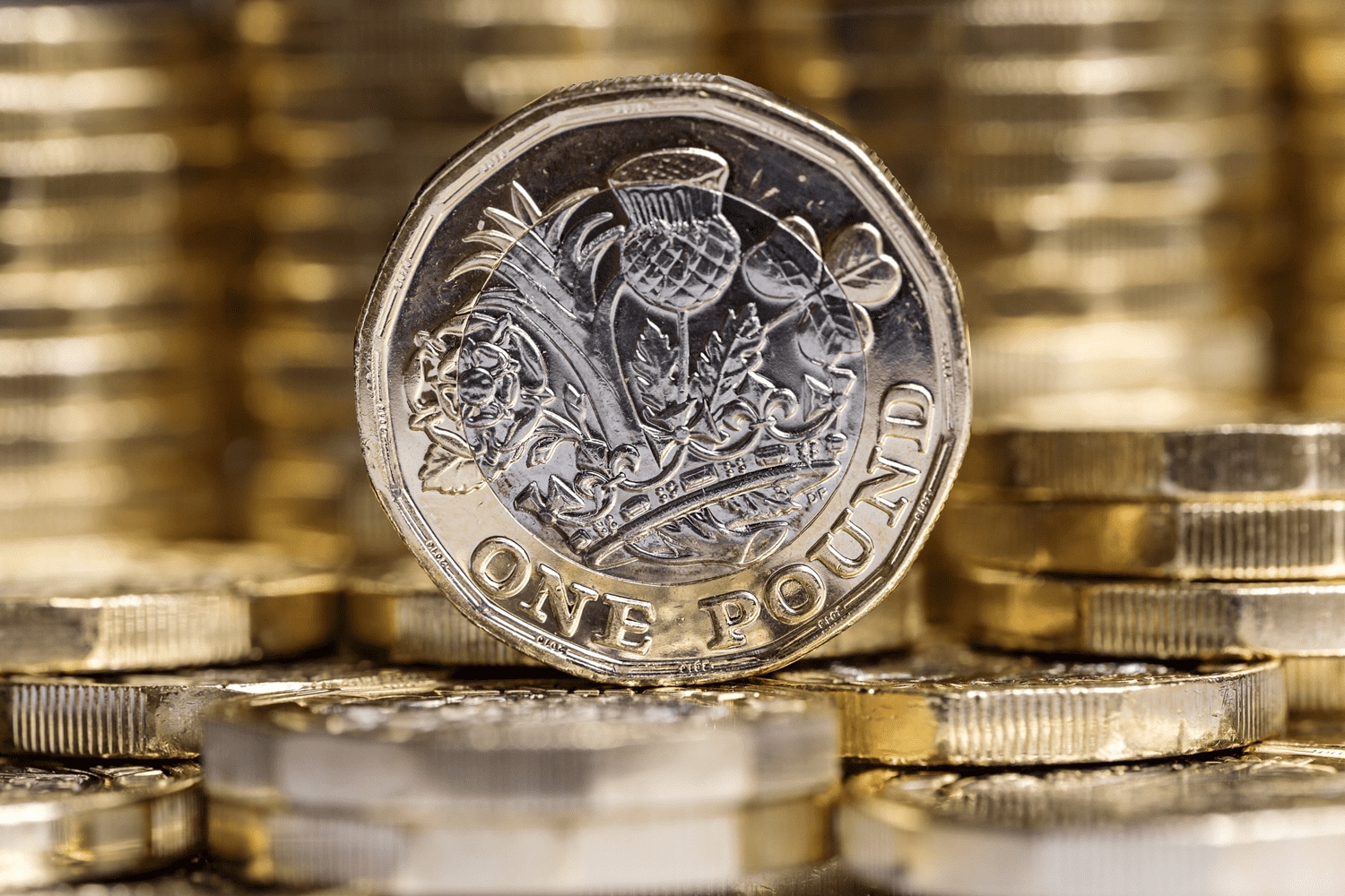 a new one pound coin standing on its edge, on top of a pile of new one pound coins