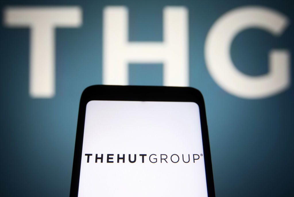 THG share price: a sign shows the THG logo while, in front of it, a phone displays the company's original name, The Hut Group.