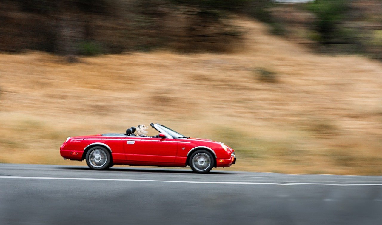 red convertible open top car driving down a road