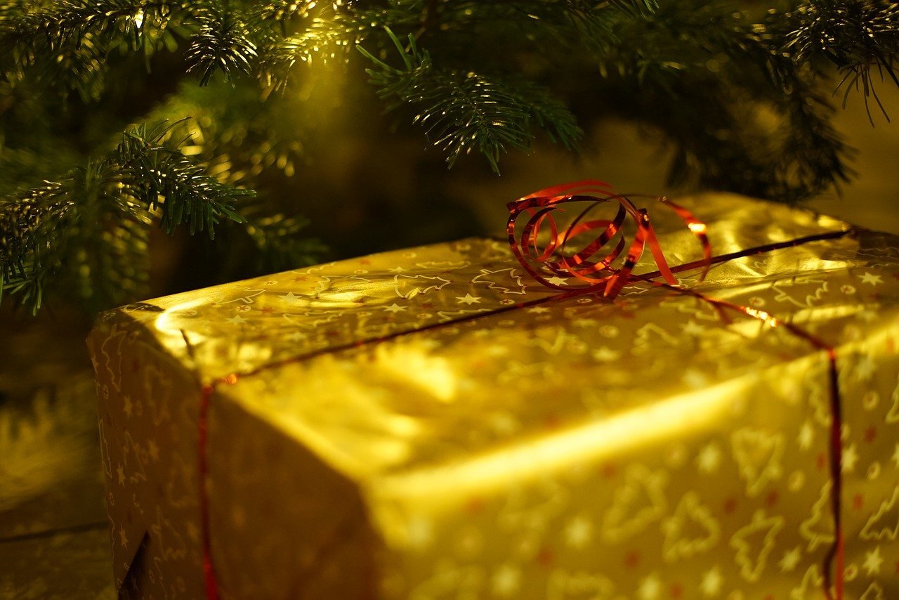 present wrapped with gold paper and red ribbon in front of Christmas tree