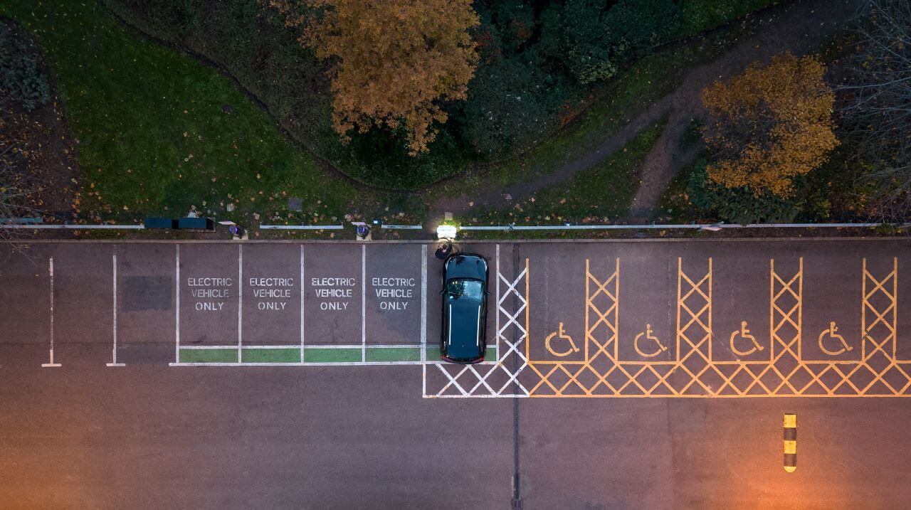 Overhead aerial view of a person connecting an electric car to an electrical vehicle charging station at dusk