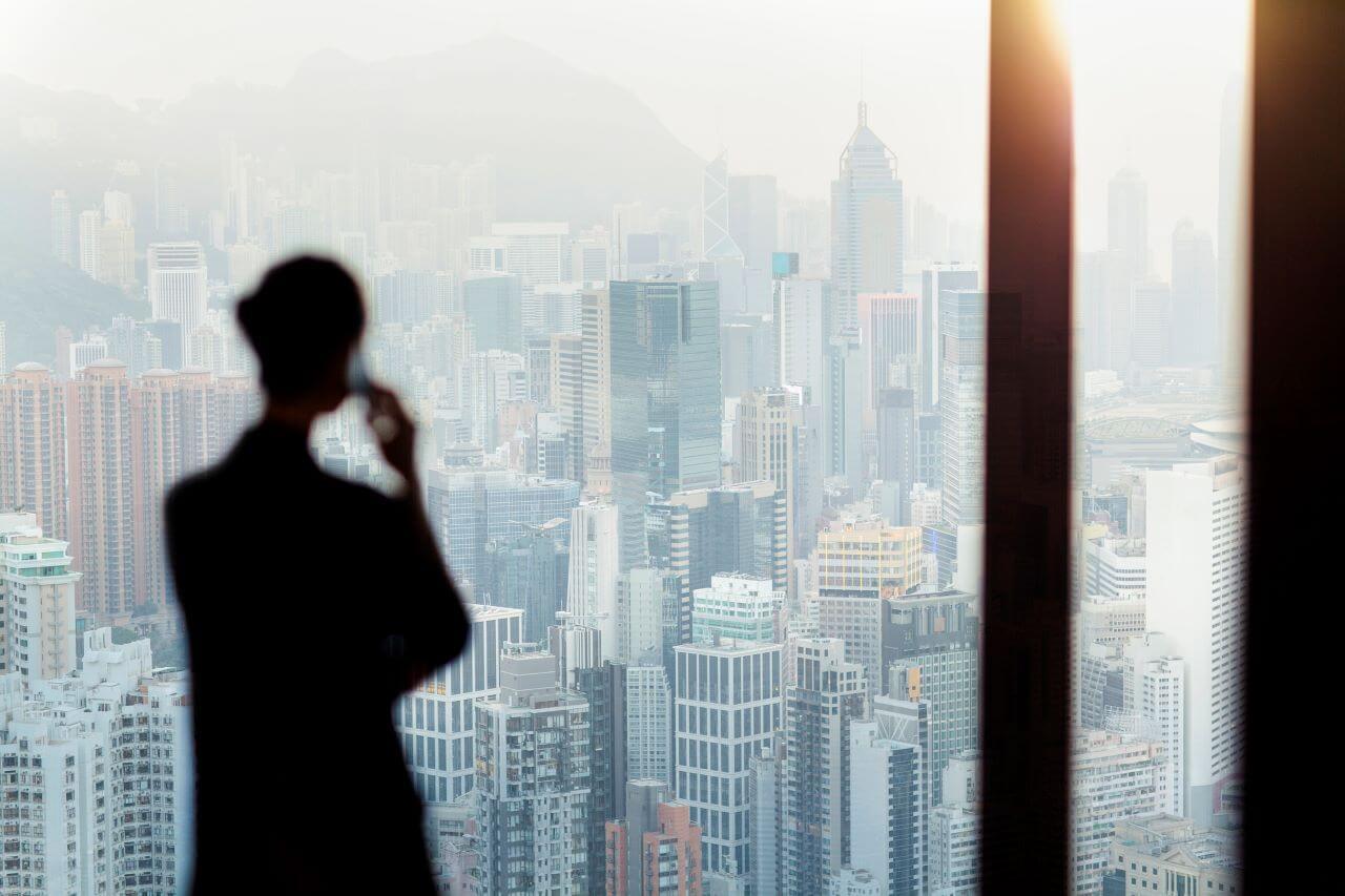 Businesswoman talking on phone from office window with Hong Kong cityscape view