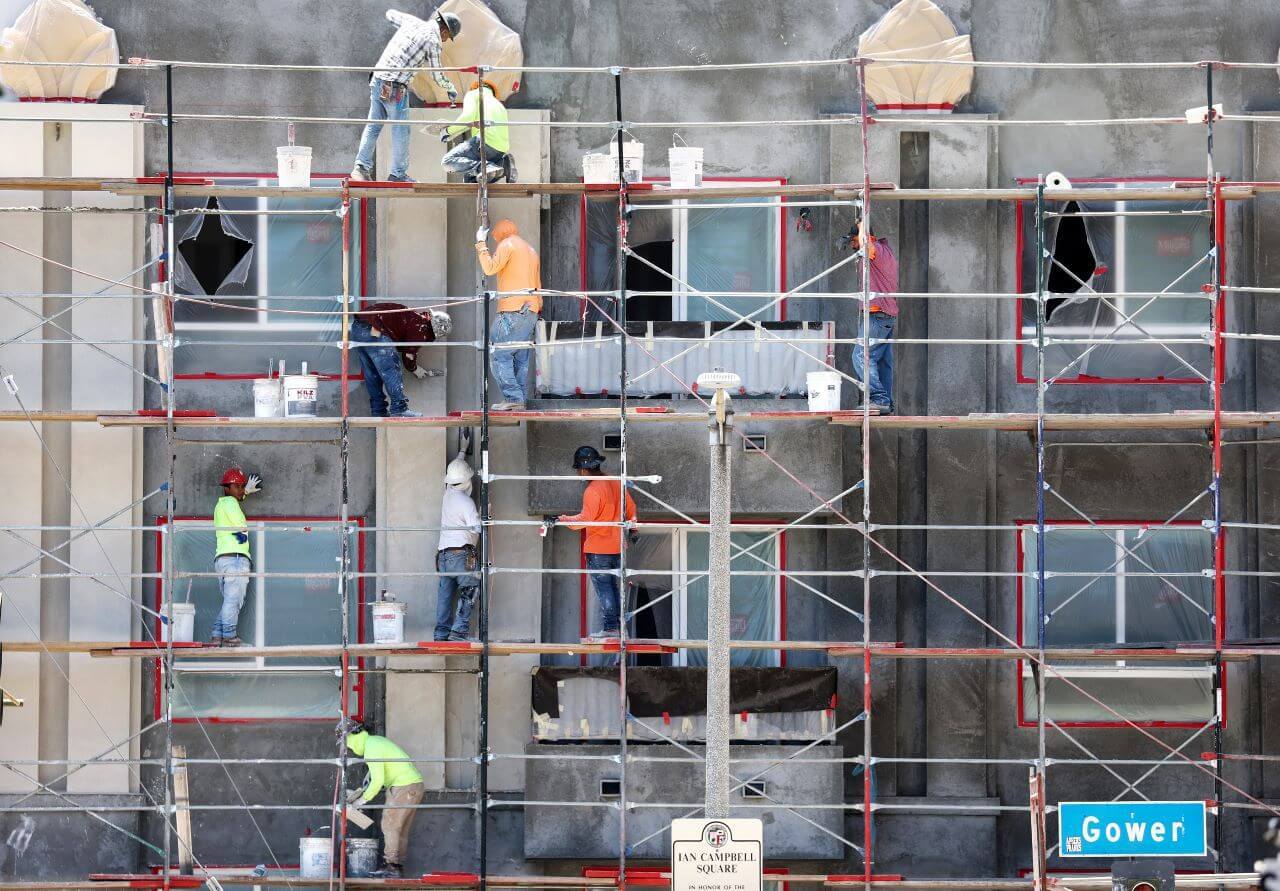 Construction workers stand on scaffolding while building residential housing