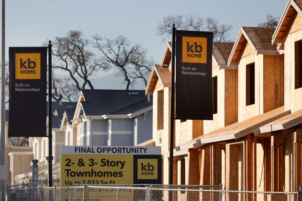 A row of homes under construction appear next to flags bearing the name of developer KB Home.
