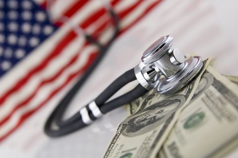 A stethoscope over a pile of dollars, with the earpieces on an American flag.